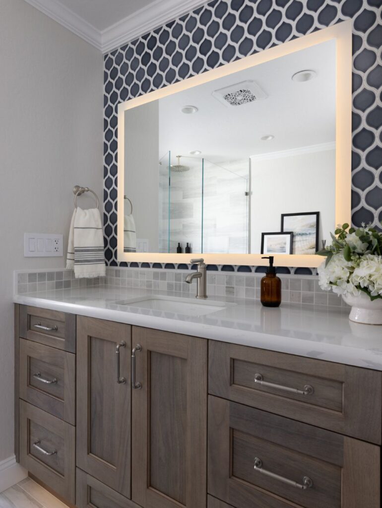 Bathroom vanity showing a blue and white backsplash, large mirror with backlighting and contemporary design