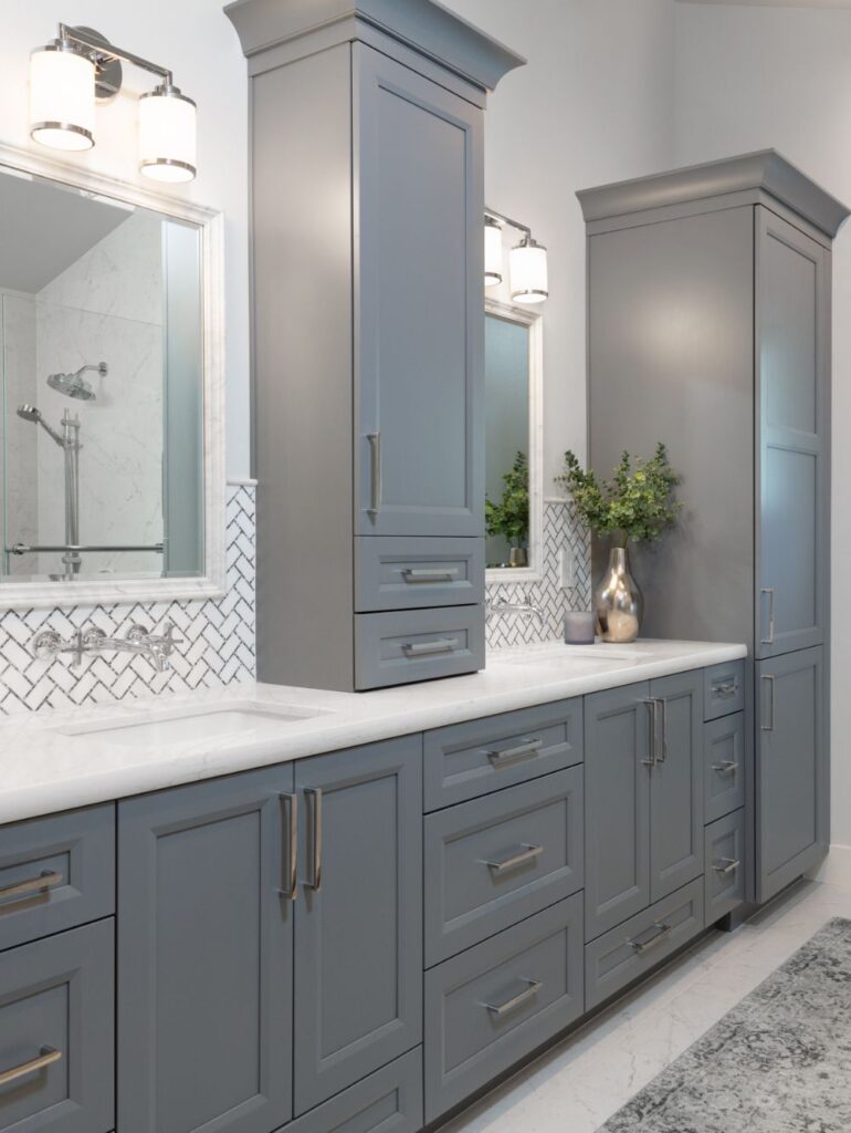 Double bathroom vanity with grey cabinetry, white marble countertops, and a white herringbone tile backsplash.