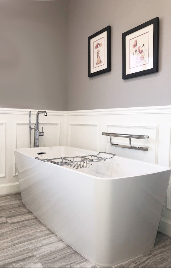 A freestanding white bathtub with a chrome faucet and caddy, positioned against a paneled wall with two framed floral prints and a towel bar.